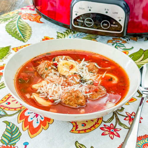 Close-up of meatball tortellini soup with spinach, carrots, tomatoes, and Parmesan cheese