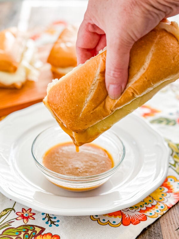 Turkey French dip sandwich being dipped into warm herb gravy
