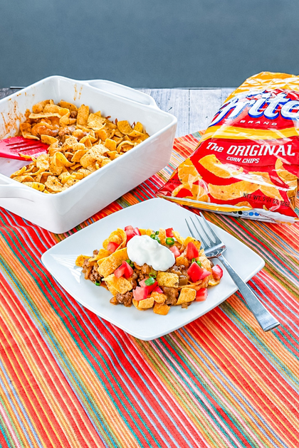 Serving of Baked Frito Pie topped with sour cream, tomatoes, and green onions