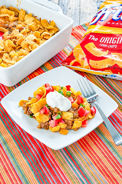 Baked Frito Pie topped with melted cheese, Fritos, sour cream, tomatoes, and green onions