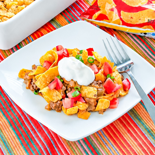 Frito pie casserole topped with shredded cheese and corn chips