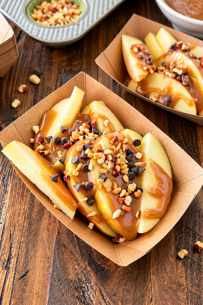 Caramel apple slices topped with chocolate chips and chopped nuts in a paper food tray