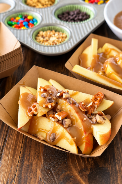 Gourmet caramel apple bar with sliced apples, homemade caramel sauce, and assorted toppings in a muffin tin