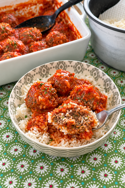 Saucy meatballs served over white rice with the baking dish and rice pot in the background