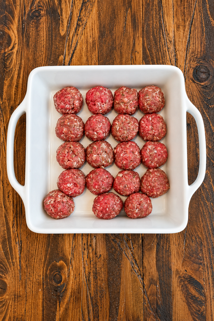 Raw meatballs with rice arranged in a white baking dish before cooking