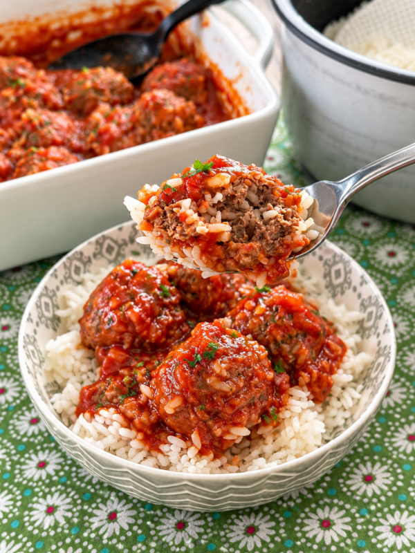 Close-up of a bite of meatball and rice with tomato sauce on a fork