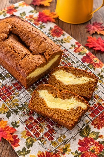 Slice of pumpkin cream cheese bread with a thick cream cheese layer next to the loaf of bread