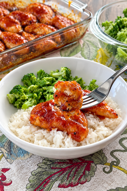 Sweet sticky chicken tenders served over white rice with steamed broccoli and a fork holding a bite of chicken