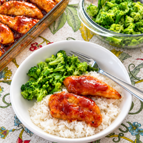 Sweet sticky chicken served over white rice with steamed broccoli, with more chicken and broccoli in the background